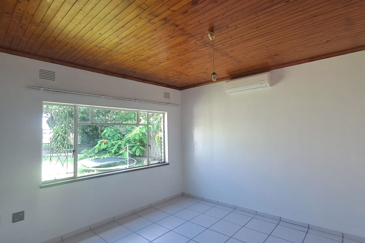 A bright, empty bedroom featuring a warm timber ceiling, tiled flooring, and a wall-mounted split-system air conditioner.