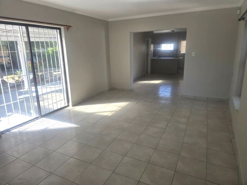 Spacious open-plan living area featuring neutral tiled flooring and a large sliding glass door with security gate, providing access to the outdoor space.