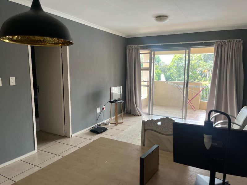 A living room featuring tiled flooring, grey painted walls, and a sliding glass door providing access to an outdoor balcony area.