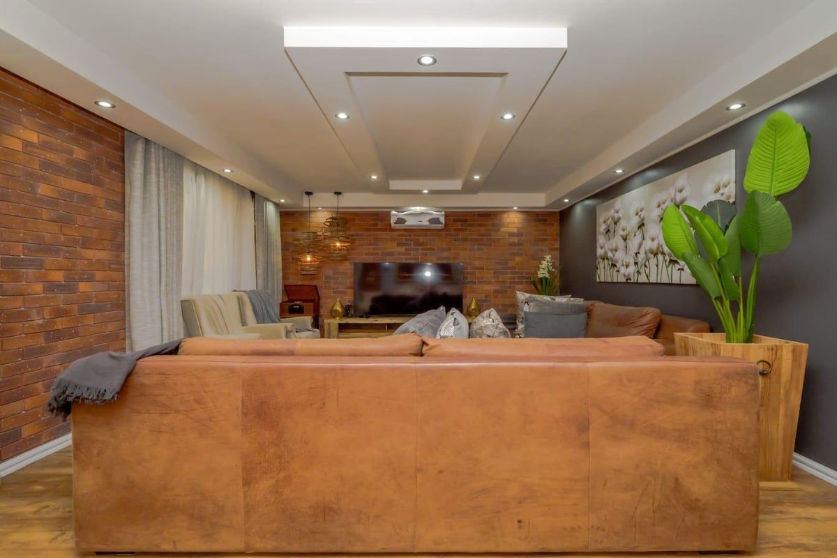 Spacious living room featuring a feature brick wall, recessed tray ceiling with downlighting, and wood-look flooring.