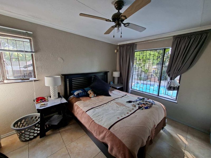 A bedroom featuring tiled flooring, a ceiling fan, and security bars on the windows with views of the pool area.