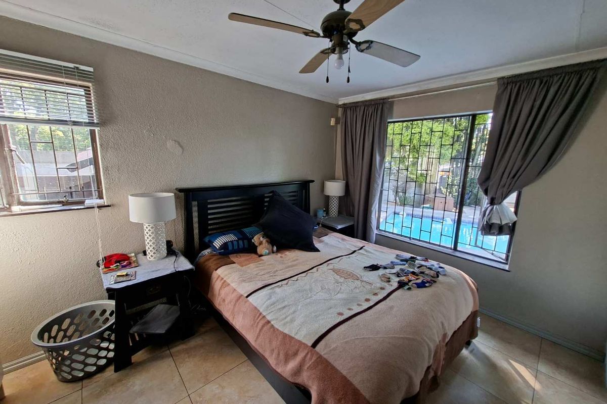 A bedroom featuring tiled flooring, a ceiling fan, and security bars on the windows with views of the pool area.
