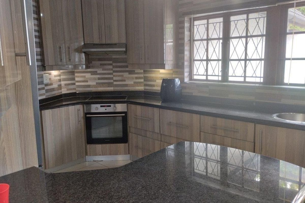 A functional kitchen featuring wood-finish cabinetry, granite countertops, a built-in oven, and a tiled backsplash with a window providing natural light.