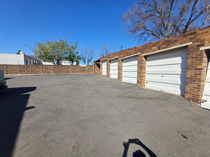 A row of brick-faced garages with white sectional doors situated in a paved parking area.