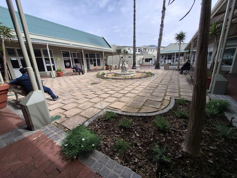 A well-maintained retail courtyard featuring paved walkways, a central water fountain, and covered access to surrounding commercial units.