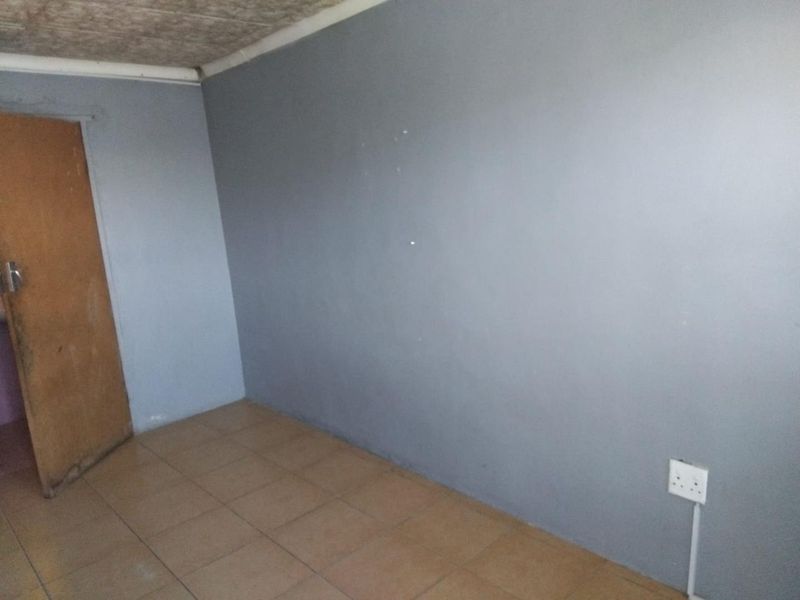 An empty bedroom featuring tiled flooring, grey painted walls, and a standard internal door, requiring cosmetic updates to improve its overall condition.