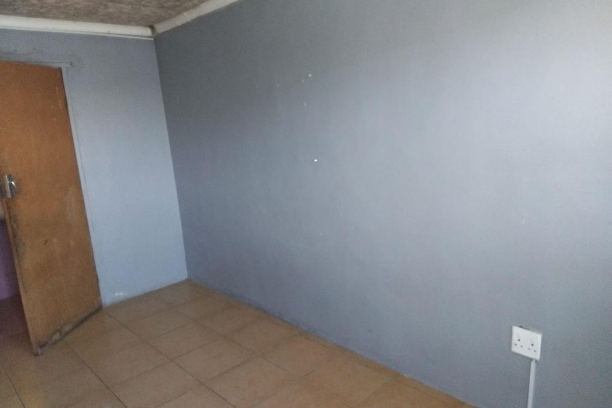 An empty bedroom featuring tiled flooring, grey painted walls, and a standard internal door, requiring cosmetic updates to improve its overall condition.