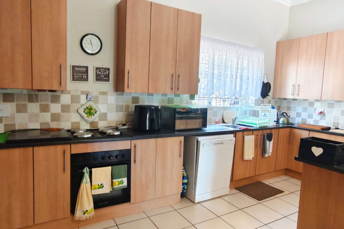 A functional kitchen featuring light wood-finish cabinetry, dark countertops, tiled splashbacks, and tiled flooring, providing ample storage and workspace.
