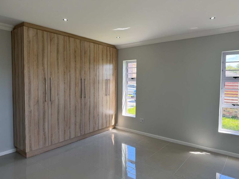 A bright, modern bedroom featuring sleek built-in wooden cupboards, polished tiled flooring, and large windows that provide ample natural light.