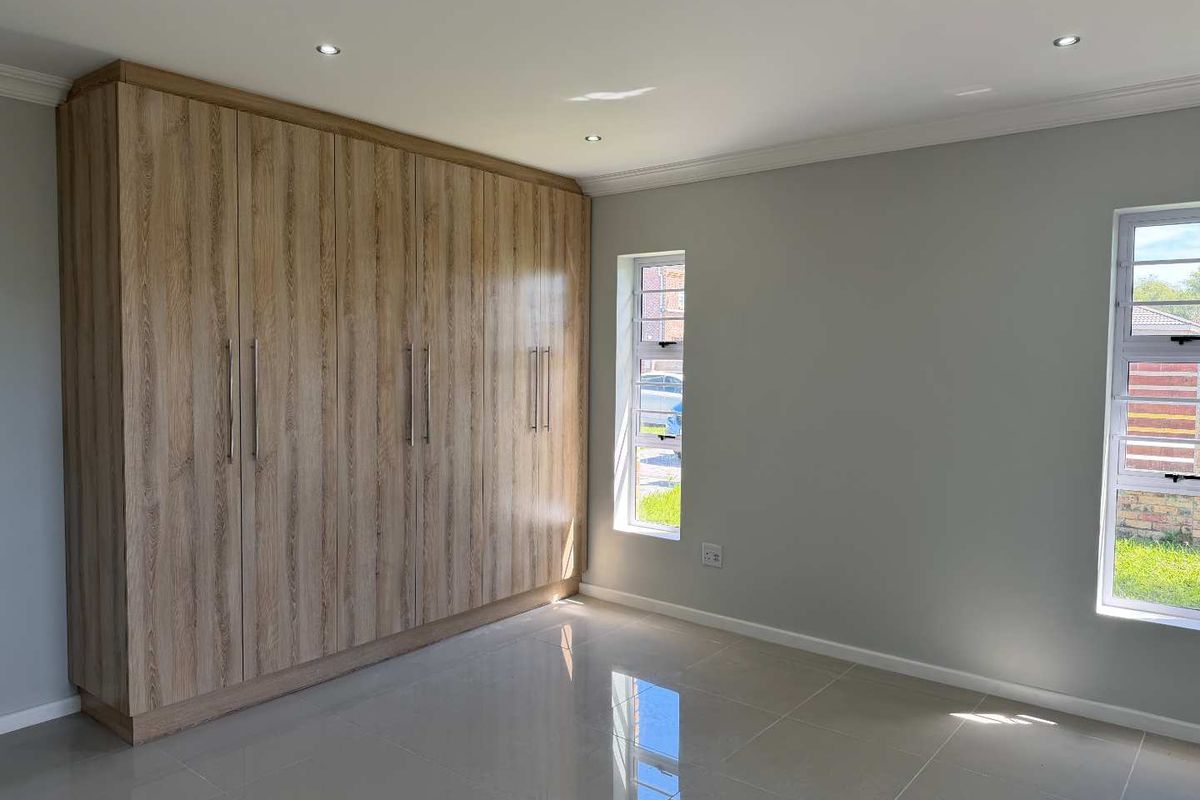 A bright, modern bedroom featuring sleek built-in wooden cupboards, polished tiled flooring, and large windows that provide ample natural light.