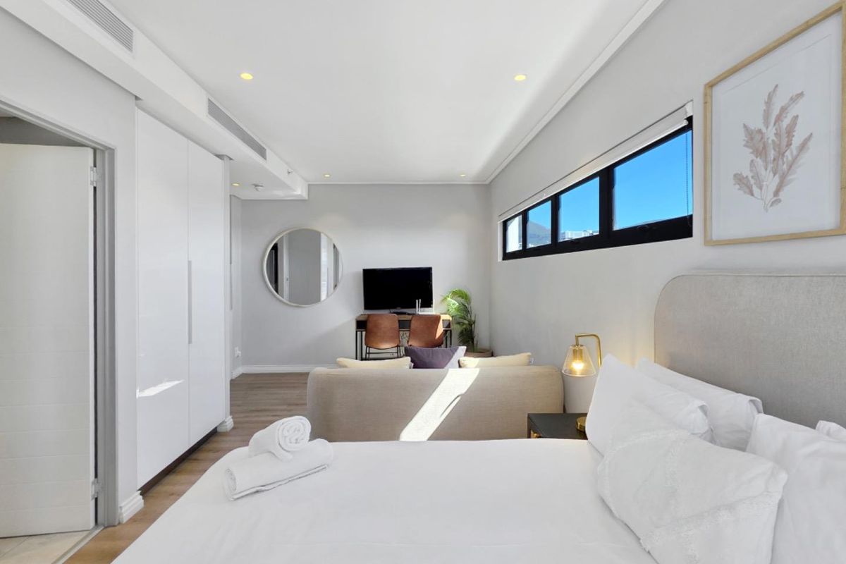 Modern bedroom featuring built-in cupboards, recessed ceiling lighting, ducted air conditioning, and horizontal clerestory windows with laminate flooring.