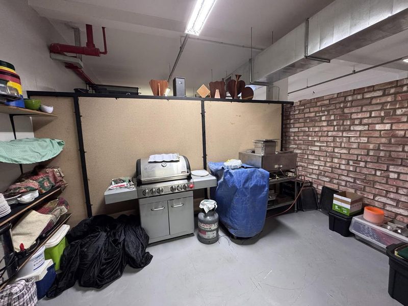 Utility space featuring exposed brickwork, industrial ducting, and concrete flooring, currently utilized as a storage and prep area.