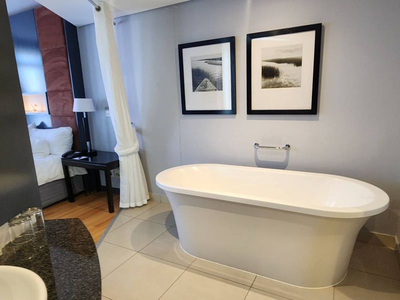 Modern bathroom featuring a sleek freestanding bathtub, granite-topped vanity basin, and neutral tiled flooring, seamlessly integrated with the adjacent bedroom area.