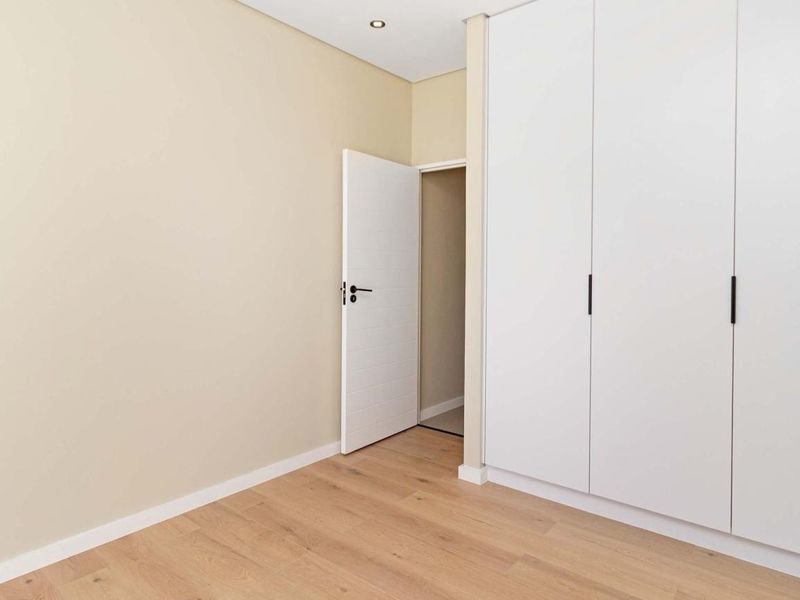 A clean, modern bedroom featuring light laminate flooring, neutral walls, and ample built-in cupboard storage.