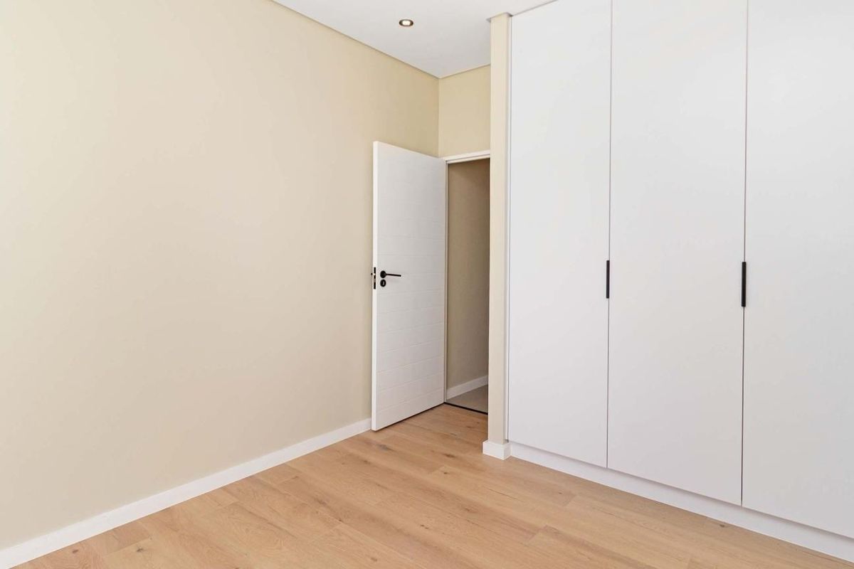 A clean, modern bedroom featuring light laminate flooring, neutral walls, and ample built-in cupboard storage.