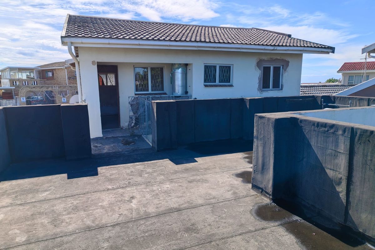 Rear view of the property featuring a flat roof terrace with parapet walls, tiled roof section, and visible exterior maintenance requirements.