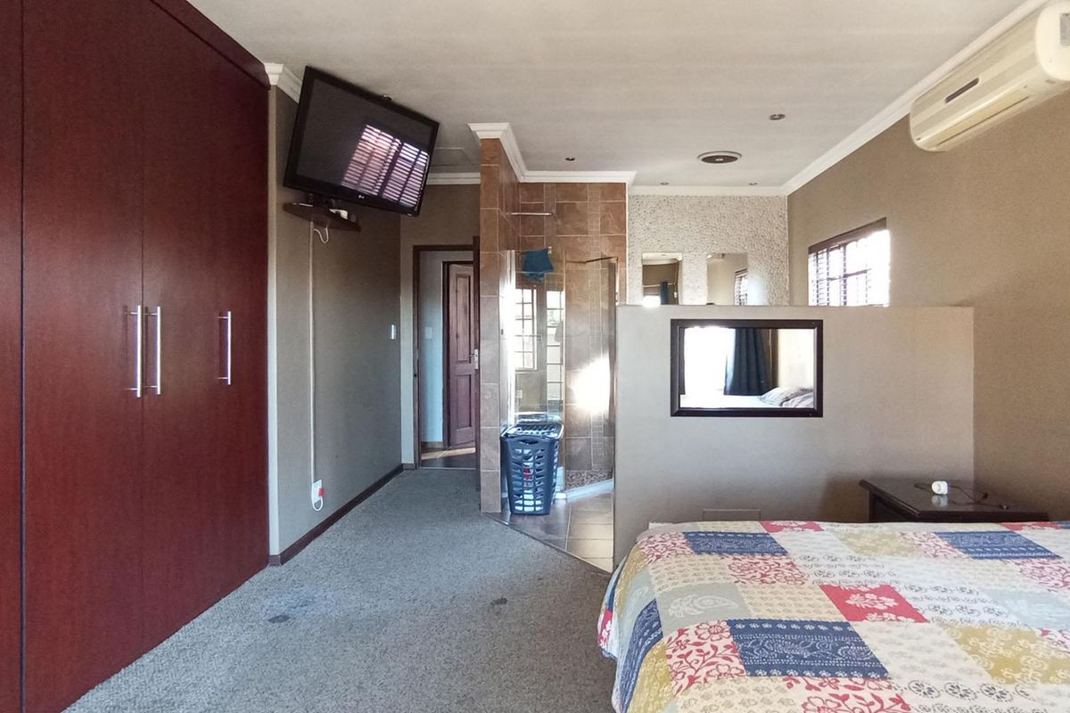 Spacious bedroom featuring built-in wooden cabinetry, an en-suite bathroom area with tiled partition, and a wall-mounted air conditioning unit.