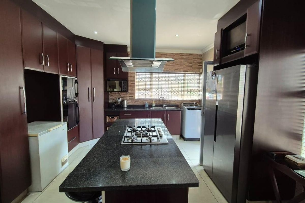 A spacious kitchen featuring dark wood cabinetry, granite countertops, a central island with a gas hob, and integrated appliances.