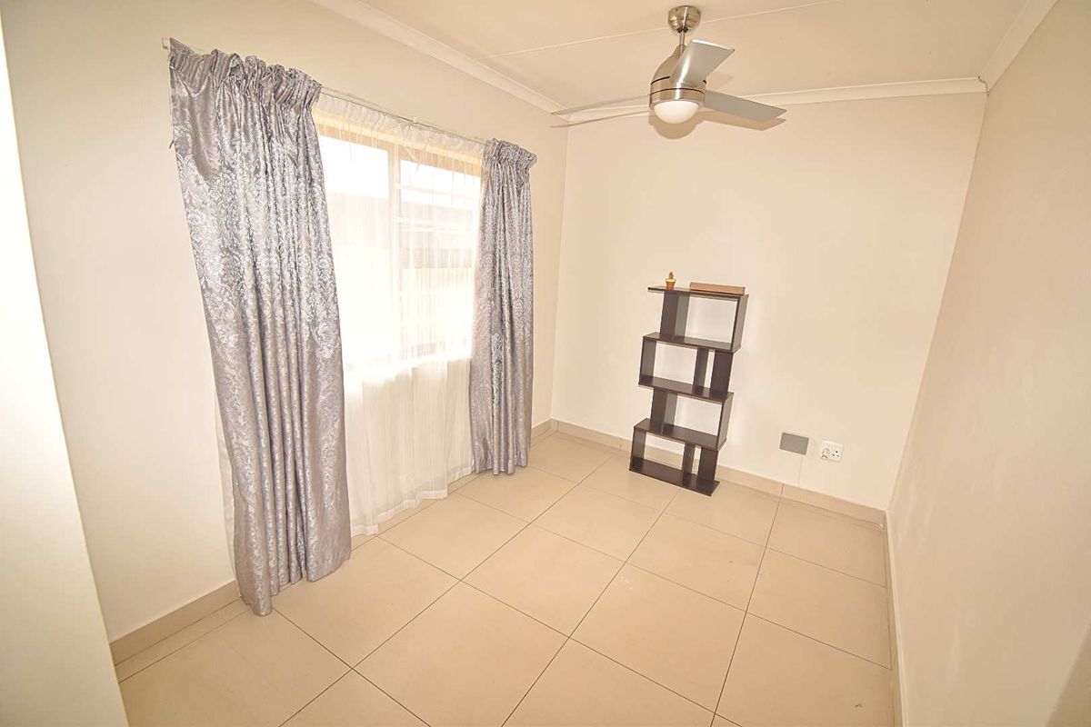 A bright bedroom featuring neutral tiled flooring, a ceiling fan, and a window with curtain tracks.