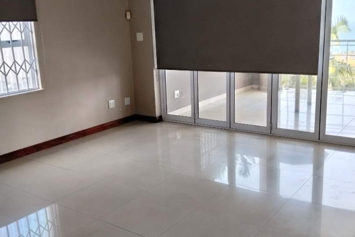 Spacious, light-filled living area featuring large format floor tiles, modern roller blinds, and sliding glass doors leading to an outdoor balcony.
