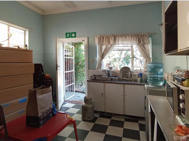 A functional kitchen featuring basic cabinetry, a gas hob, and classic checkered flooring, with direct access to the exterior via a security gate.