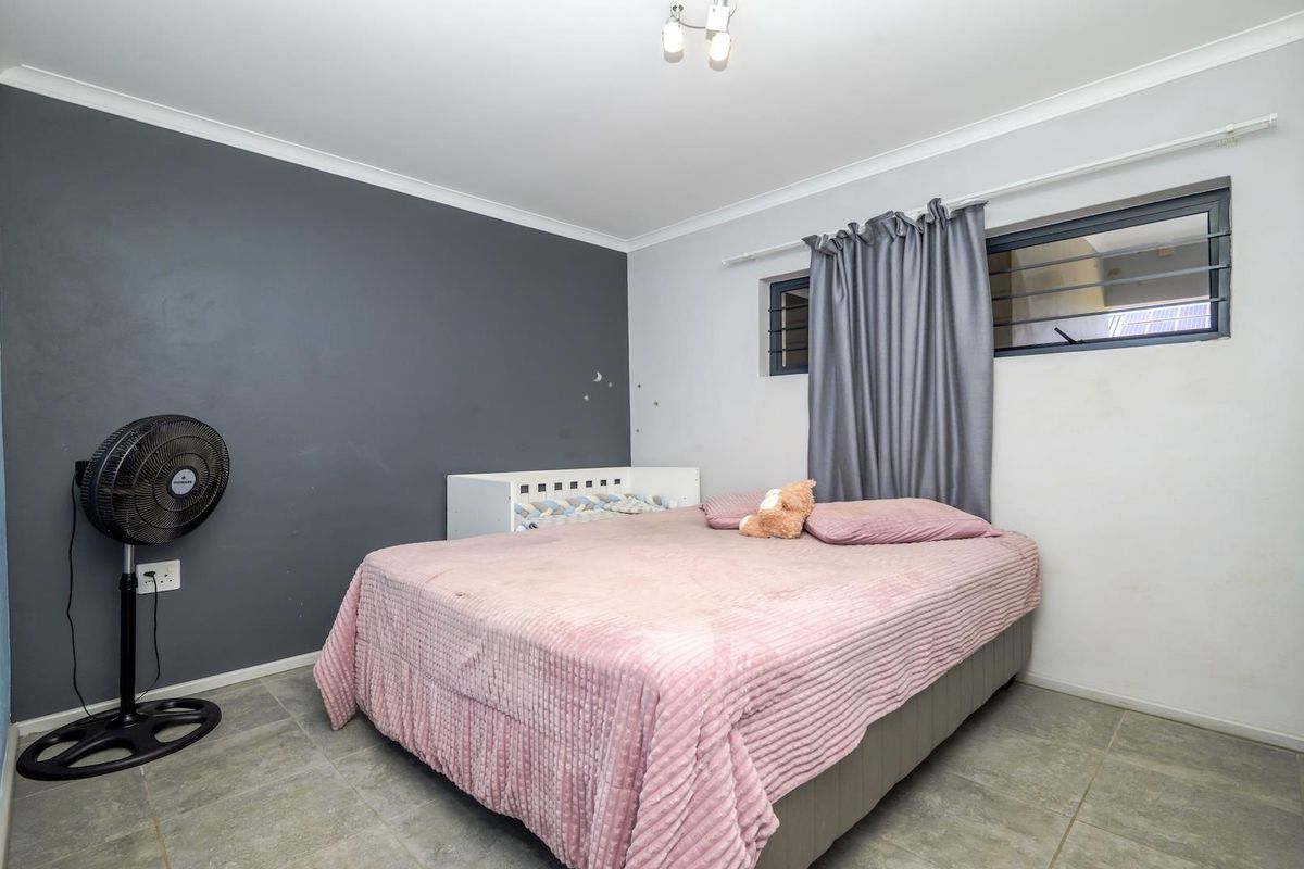 A bedroom featuring tiled flooring, a built-in cupboard, and a louvered window, with a neutral color palette and a dark grey accent wall.
