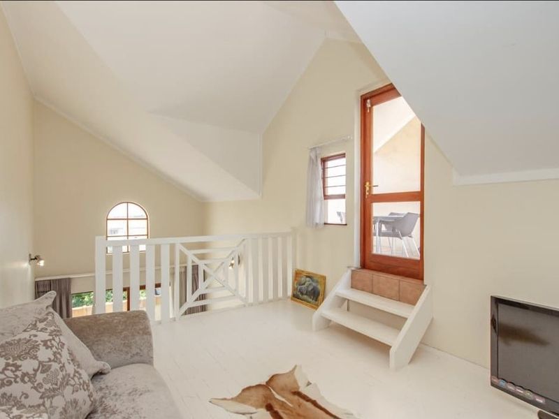 A bright living area featuring a vaulted ceiling, white wooden flooring, a mezzanine railing, and direct access to an outdoor balcony.