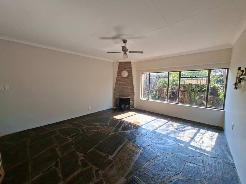 Spacious living room featuring unique flagstone flooring, a corner stone fireplace, and a large window providing natural light.