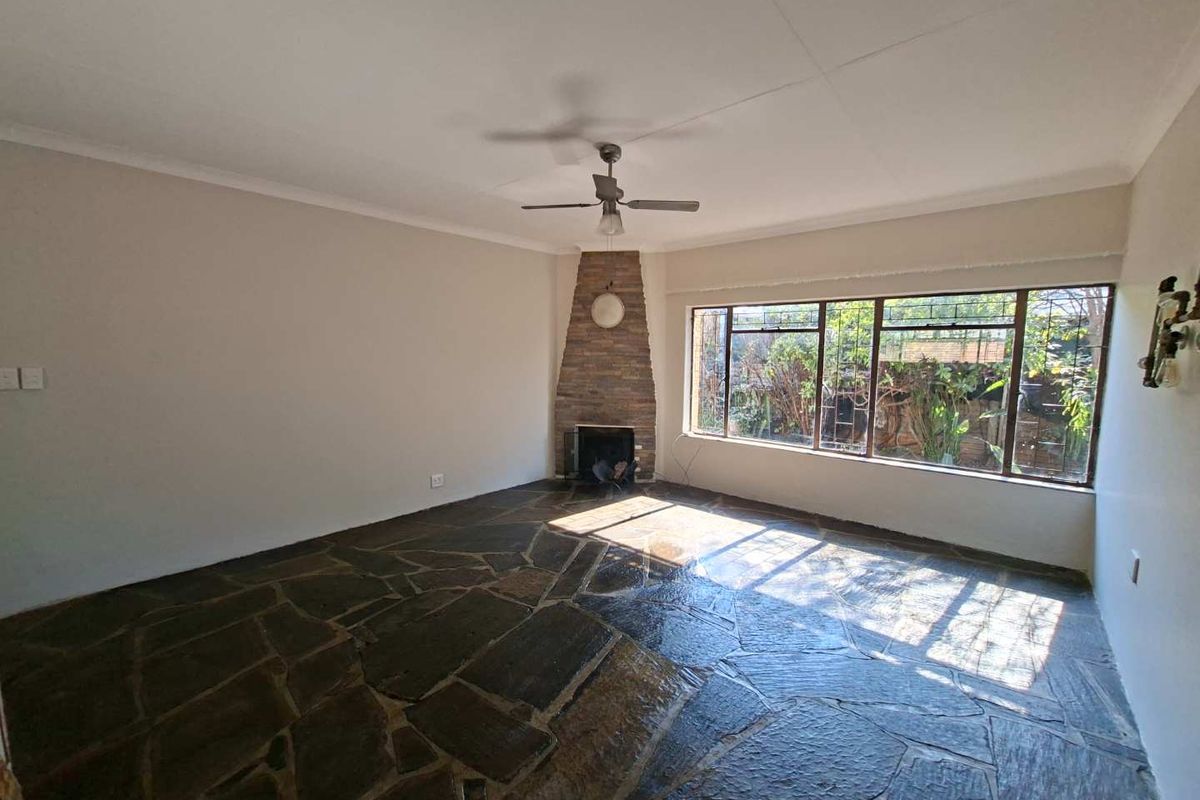 Spacious living room featuring unique flagstone flooring, a corner stone fireplace, and a large window providing natural light.