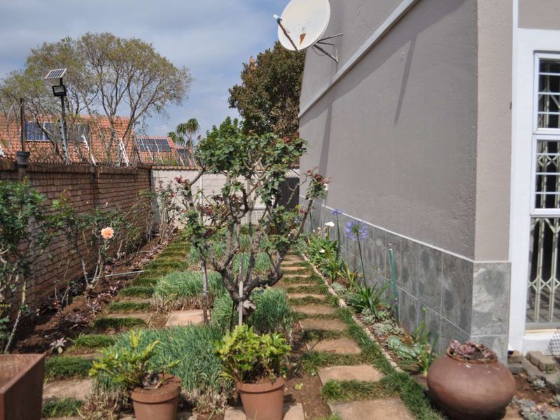 A side garden area featuring a brick boundary wall with electric fencing, stone-clad exterior wall, and paved walkway leading along the side of the townhouse.