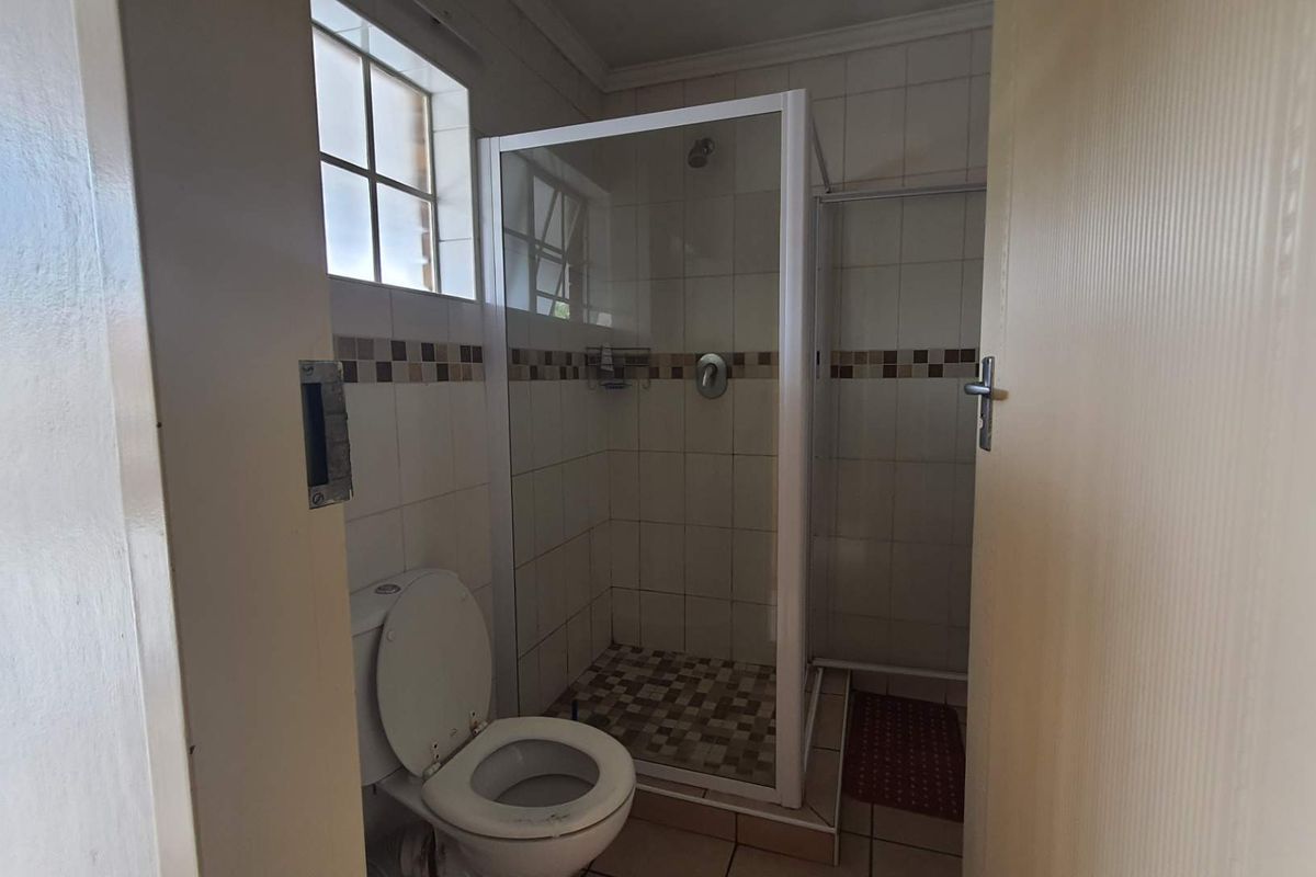 A functional bathroom featuring a tiled shower enclosure, a standard toilet, and a small window for natural light.
