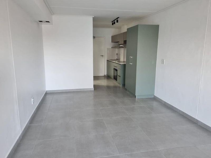 An open-plan living area featuring modern grey floor tiles and a compact, functional kitchen with built-in cabinetry and appliances.
