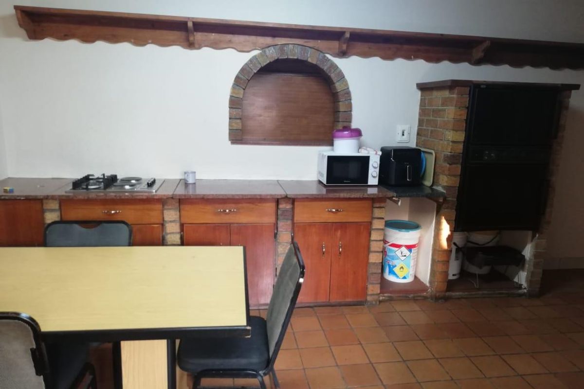 A rustic kitchen featuring built-in wooden cabinetry, a gas hob, a built-in oven, and a distinctive brick feature wall with an arched niche.