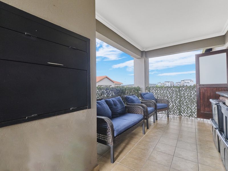 A covered balcony featuring tiled flooring and a built-in braai, offering an outdoor entertainment space with privacy screening.