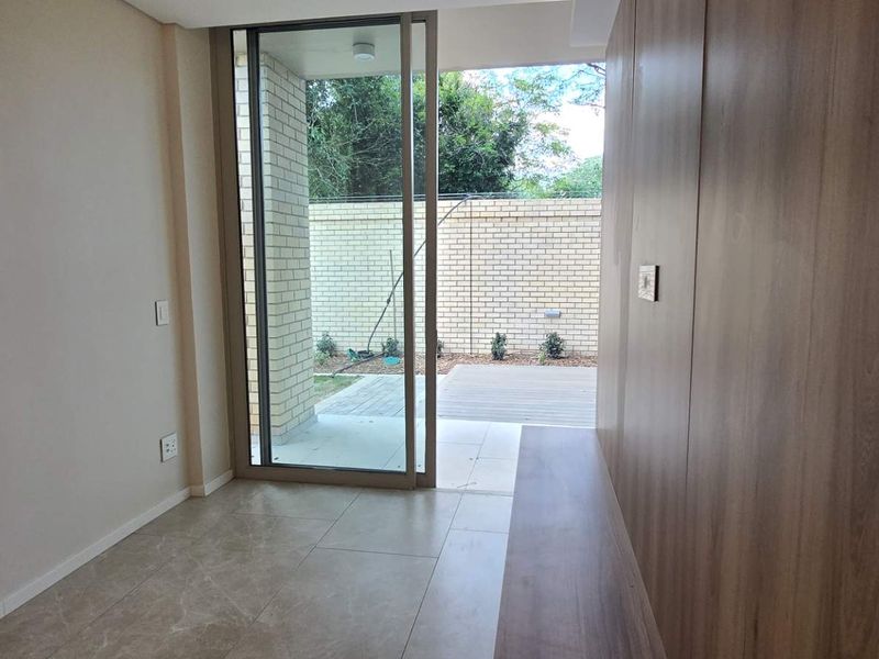 A bright, modern living area featuring sleek tiled floors, built-in cabinetry, and a large sliding glass door providing direct access to a private outdoor patio.