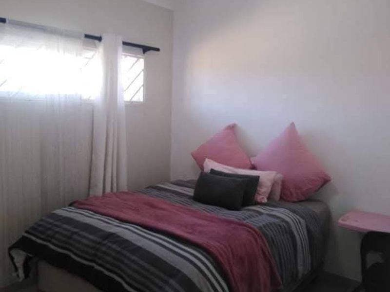 A functional bedroom featuring tiled flooring, a window with security bars, and a central ceiling light fixture.