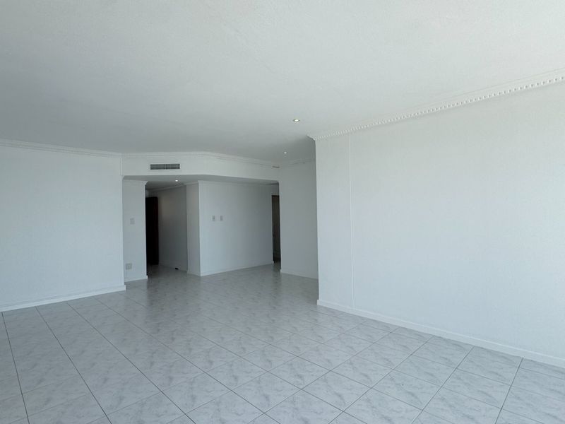 A spacious, empty living area featuring neutral ceramic floor tiles, recessed downlighting, and crown molding, providing a clean canvas for interior design.