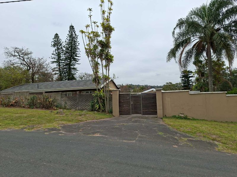 Front view of the property featuring a secure metal gate, perimeter wall, and tiled roof structure with an asphalt driveway.