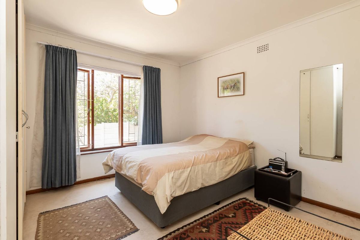 A functional bedroom featuring built-in wardrobe storage, large window with natural light, and neutral wall finishes.
