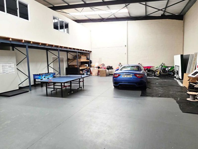 Spacious industrial utility area featuring a mezzanine level, high-level windows, exposed steel roof trusses, and durable epoxy-coated concrete flooring.