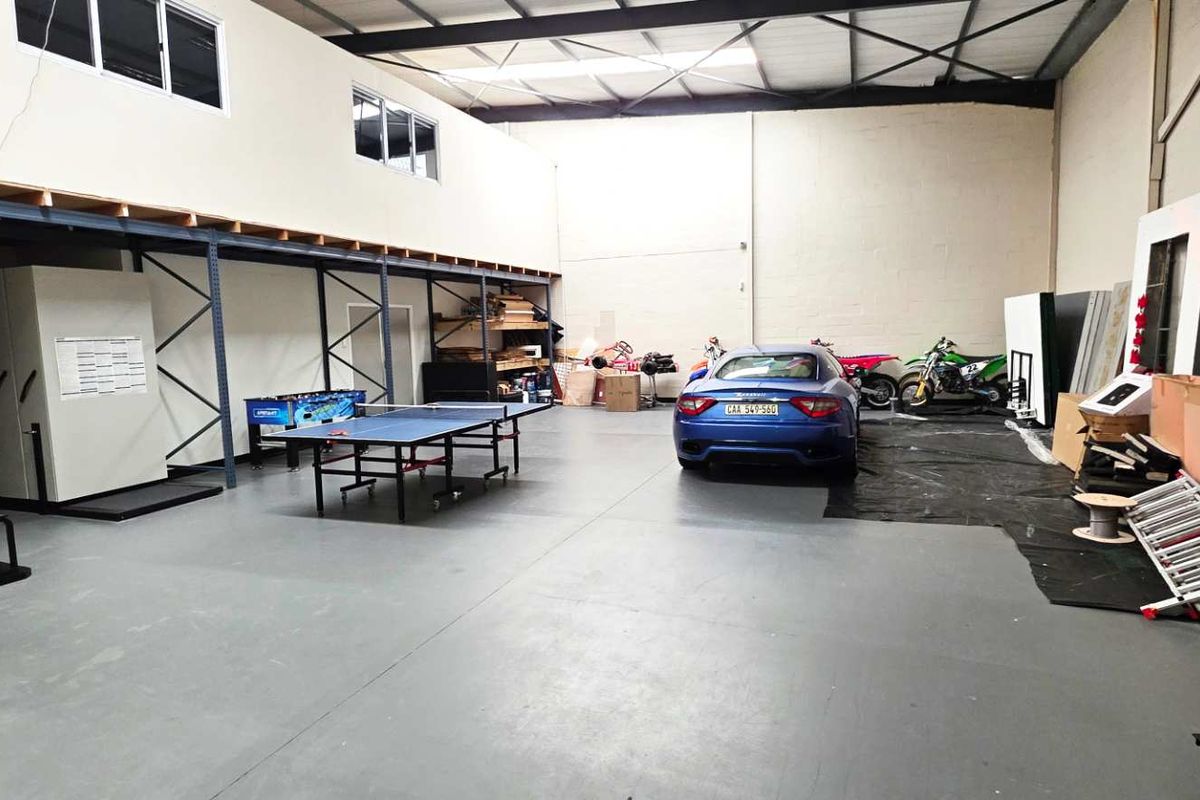 Spacious industrial utility area featuring a mezzanine level, high-level windows, exposed steel roof trusses, and durable epoxy-coated concrete flooring.
