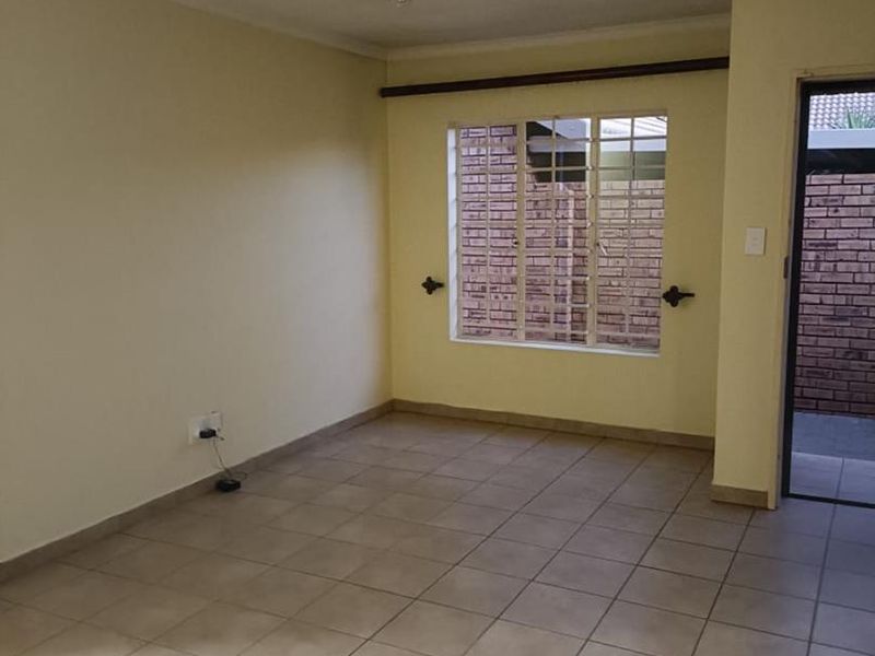 An empty, neutrally painted living room featuring tiled flooring, a window with security bars, and direct access to an exterior area.