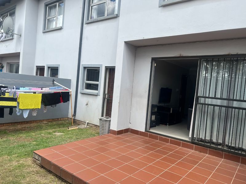 Rear view of the apartment featuring a tiled patio area, sliding glass door with security gate, and access to the small garden space.