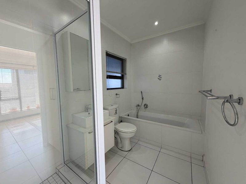 A clean, modern bathroom featuring a shower enclosure, bathtub, toilet, and vanity basin with white tiled finishes throughout.