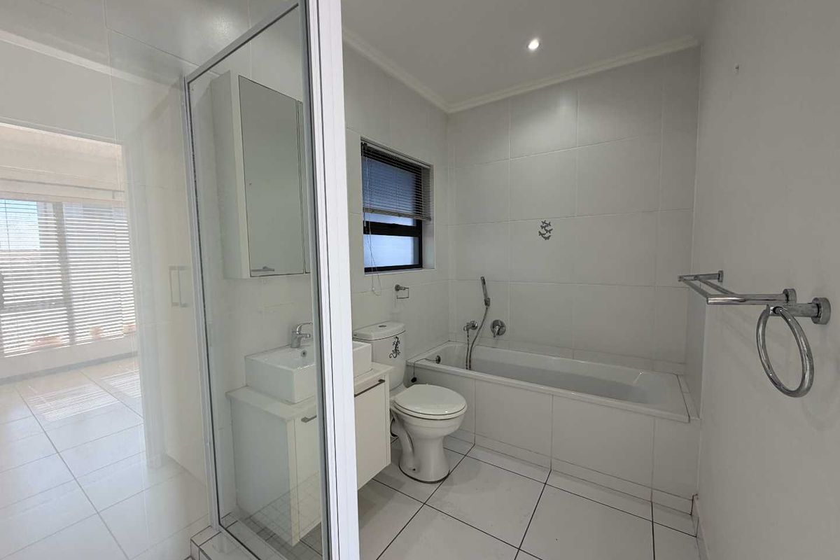 A clean, modern bathroom featuring a shower enclosure, bathtub, toilet, and vanity basin with white tiled finishes throughout.