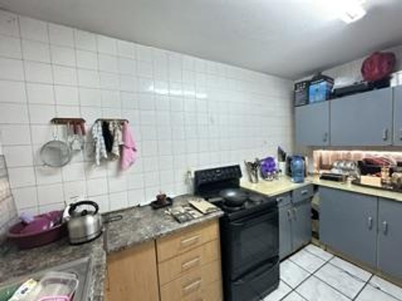 A functional kitchen featuring tiled walls, laminate countertops, and built-in cabinetry, offering a practical layout with a freestanding stove.