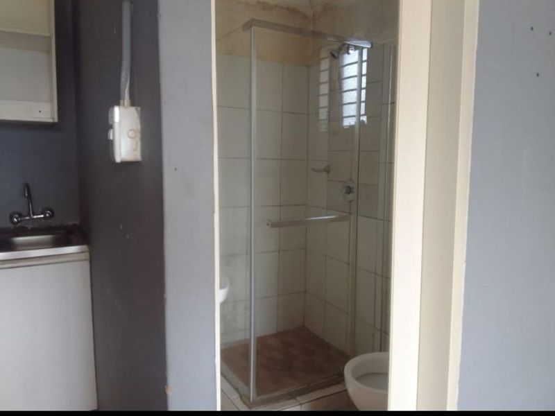A compact bathroom featuring a shower enclosure, toilet, and sink, requiring cosmetic updates and repairs to wall and floor finishes.