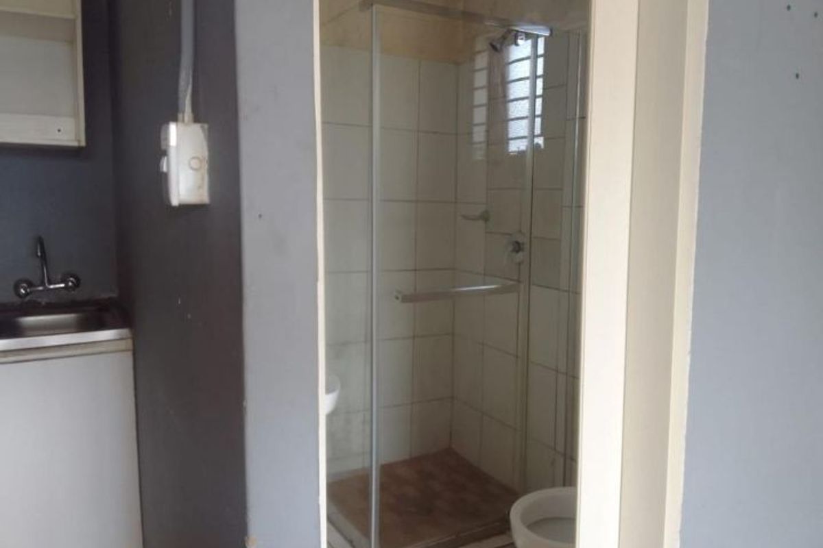 A compact bathroom featuring a shower enclosure, toilet, and sink, requiring cosmetic updates and repairs to wall and floor finishes.