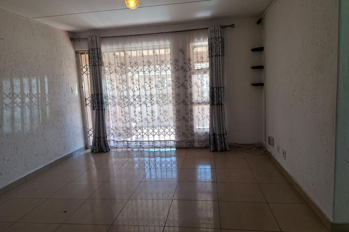 A spacious living room featuring tiled flooring, textured walls, and a large sliding door with security gate leading to the exterior.