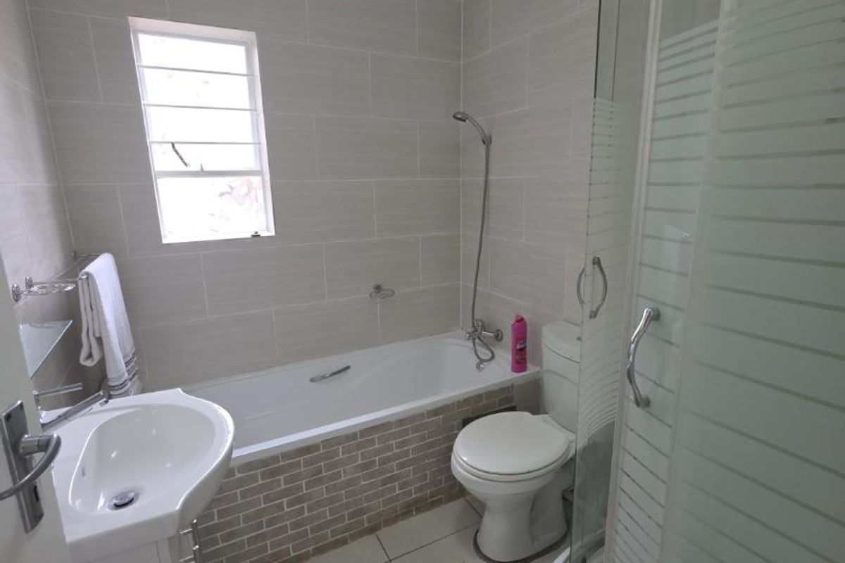 A functional bathroom featuring a bathtub, separate shower enclosure, vanity basin, and toilet with neutral wall and floor tiling.